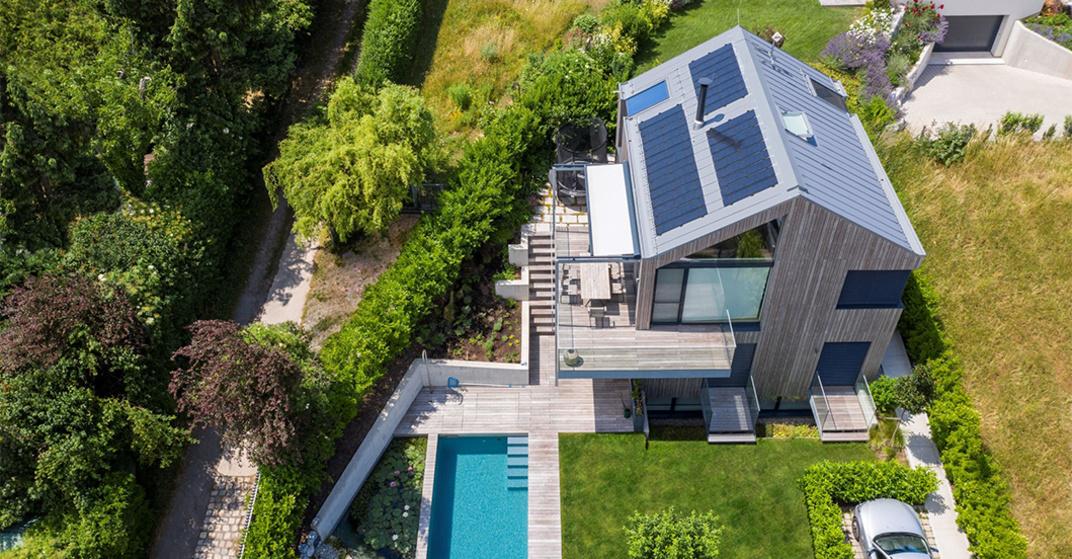 Vogelperspektive eines modernen Einfamilienhauses mit PV-Modulen am Zinkdach und einem Pool im Garten