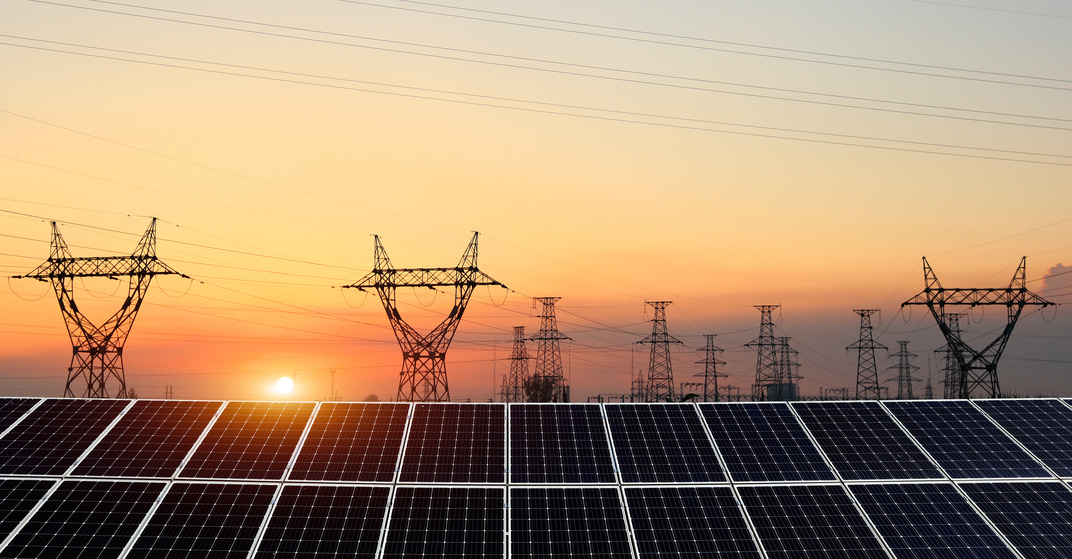 große Photovoltaikanlage mit vielen Paneelen und Strommasten im Hintergrund im Sonnenuntergang
